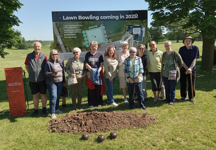 Lawn bowlers gather in front of site plan at ground breaking ceremony